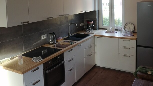 Une cuisine moderne avec des meubles blancs, une cuisinière noire et un plan de travail en bois.