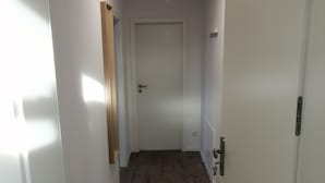 Un couloir avec un plancher en bois, des murs blancs et une porte au fond.