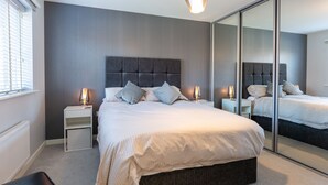 A modern bedroom with a large bed, bedside tables, a mirror, and a window with blinds. - Luxury detached house next to Gedling Country Park. Pet friendly! (Nottingham)