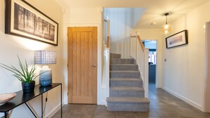 A hallway with a wooden door, a staircase, and a console table with a lamp and plant. - Luxury detached house next to Gedling Country Park. Pet friendly! (Nottingham)