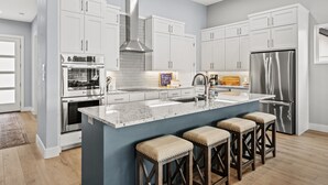 A modern kitchen with white cabinets, stainless steel appliances, and a central island with bar stools. - Spectacular, New Waterfront Home.  A Place to Escape and Enjoy Lake Life! (Mabank)