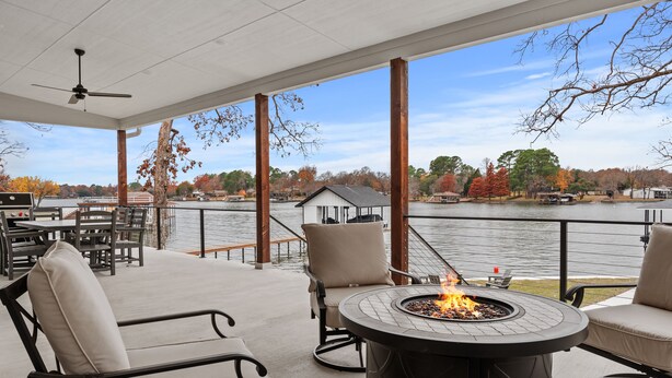 A covered patio with outdoor seating, a fire pit, and a view of a lake with boats and a dock. - Spectacular, New Waterfront Home.  A Place to Escape and Enjoy Lake Life! (Mabank)