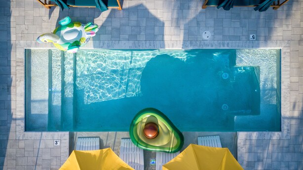 Vue aérienne d’une piscine rectangulaire, avec un jacuzzi, des parasols jaunes et des chaises longues.