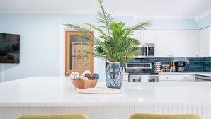 Une cuisine moderne avec des meubles blancs, un îlot central agrémenté d’une plante et d’objets décoratifs, et un four à micro-ondes placé au-dessus de l’îlot.