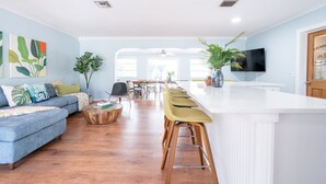 Un salon moderne avec un canapé bleu, une table basse en bois et un coin cuisine doté d’un comptoir blanc et de tabourets de bar.