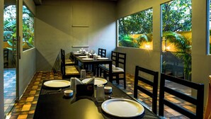 Un espace repas avec des tables dressées, de grandes fenêtres offrant une vue sur la verdure et un sol à motifs à carreaux.