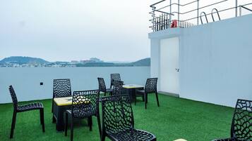 Una terraza con césped artificial, sillas de metal negro y una mesa. Se ve una pared blanca y una barandilla metálica.