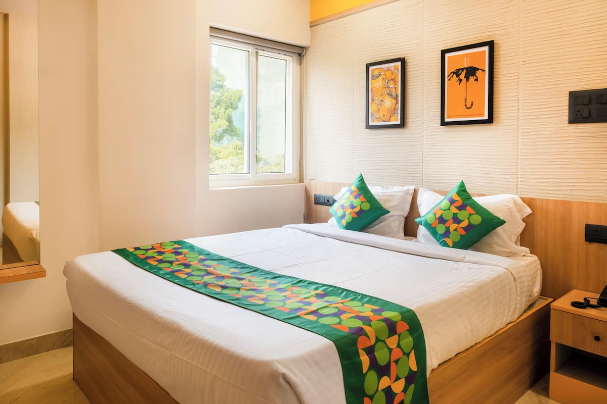 Een netjes opgemaakt bed met een kleurrijk sprei en kussens, een nachtkastje met een telefoon, en twee ingelijste foto’s aan de muur.