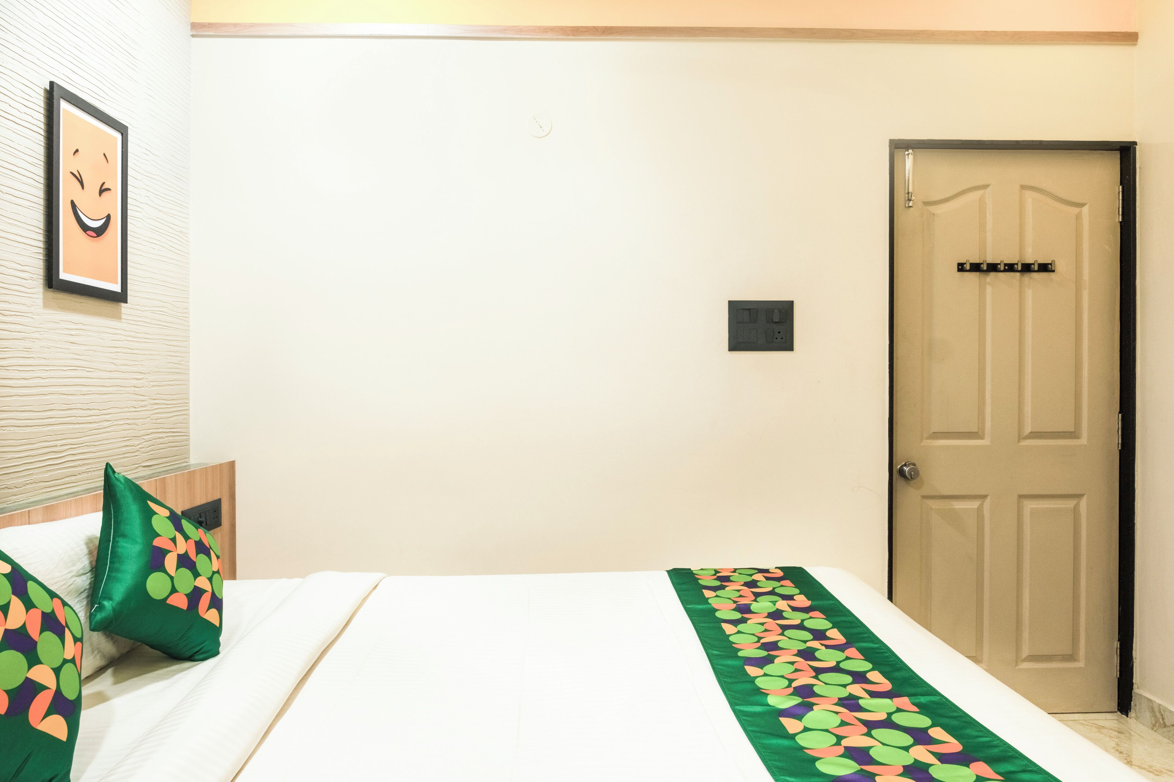 A hotel room with a bed, a door, and a wall-mounted light switch.