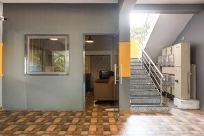 A hotel lobby with a checkered floor, a glass door leading to a seating area, and a staircase with a metal railing. - Treebo Breeze Way Rushikonda with Swimming Pool (Visakhapatnam)