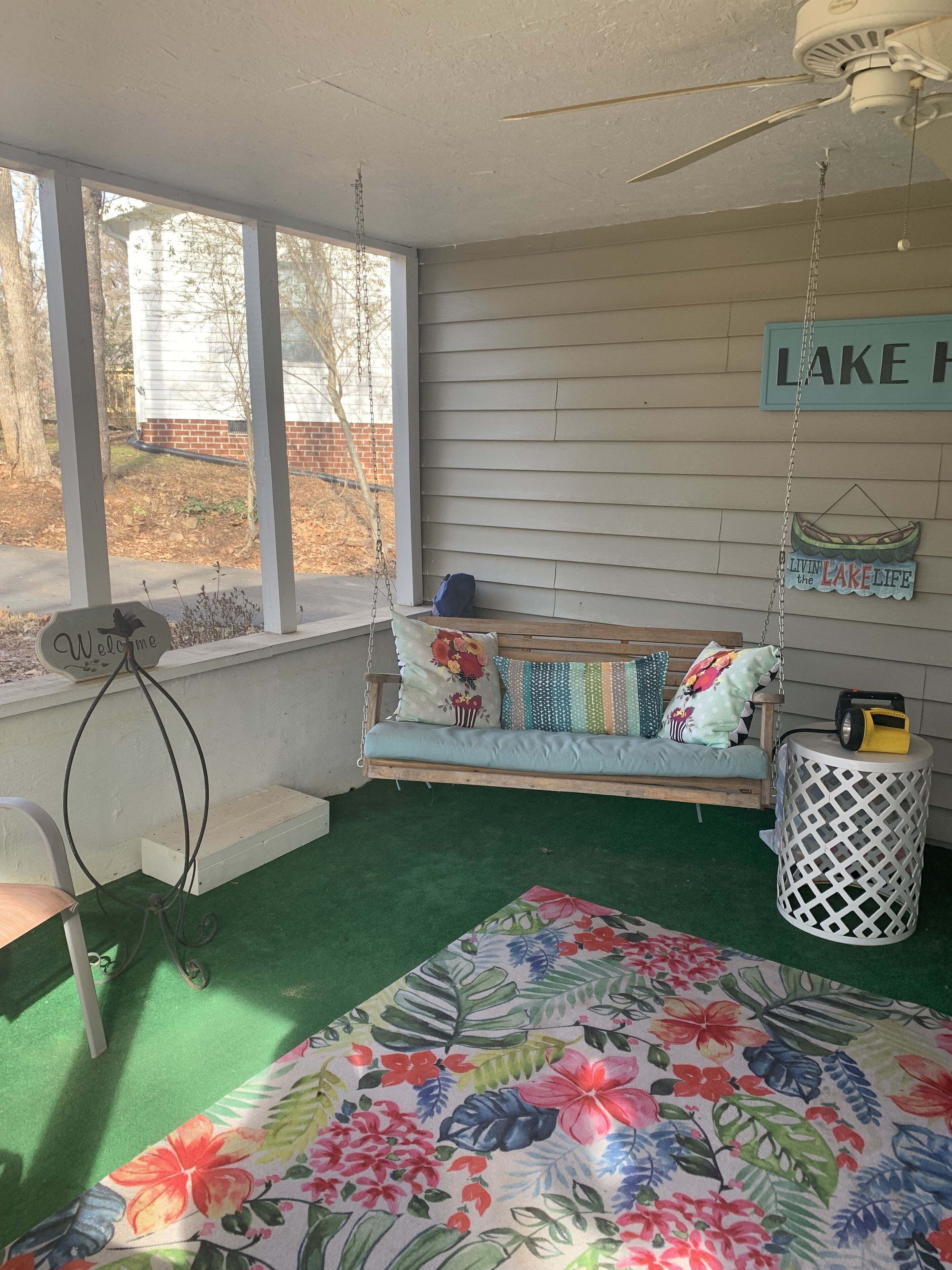 A cozy room with a swing seat, a welcome sign, and a 'Living in the Lake Life' sign.