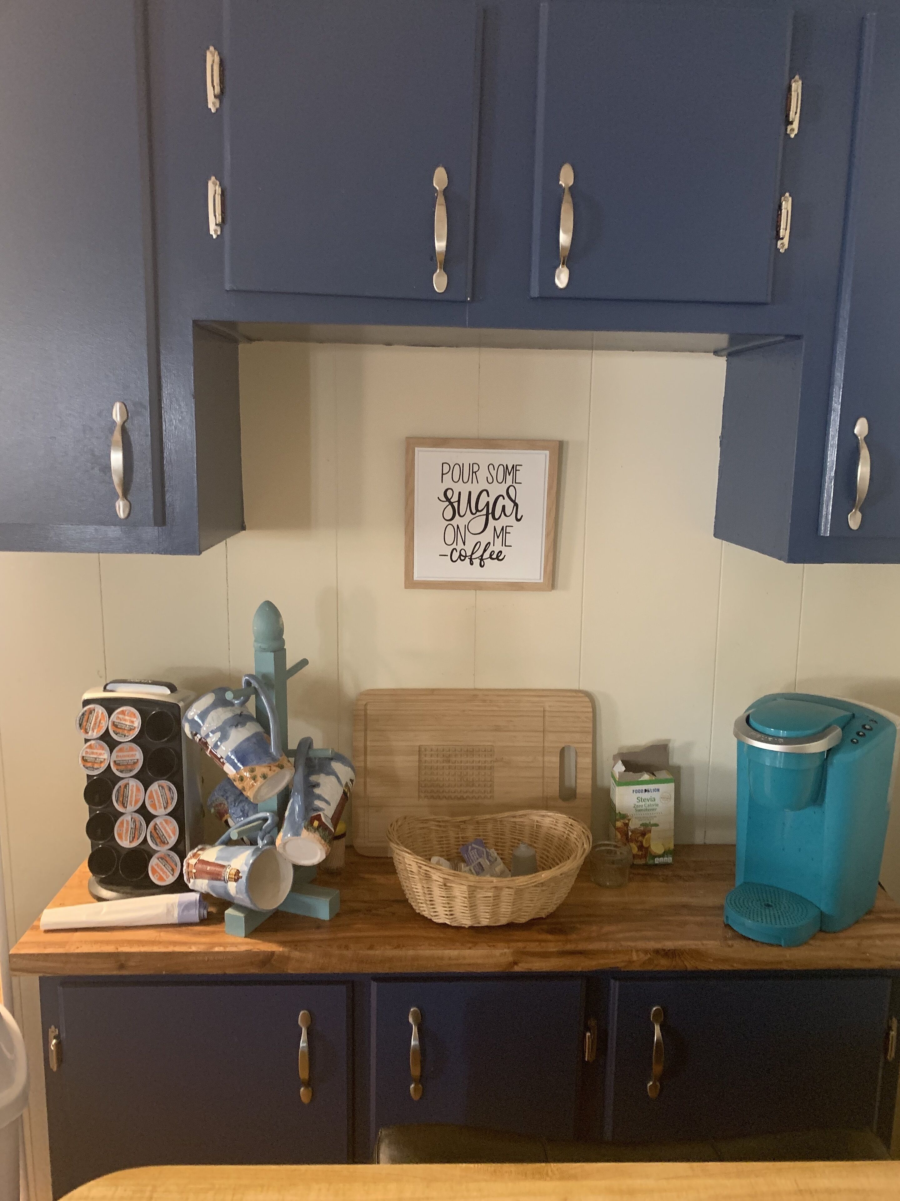 Une cuisine avec des meubles de couleur bleu foncé, une machine à café, un grille-pain et un panier posé sur le comptoir.