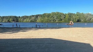 A sandy beach with a clear blue sky, a few people, and a boat in the distance. - Waterfront Lake Gaston Retreat with beautiful views, Gameroom and covered deck. (Bracey)