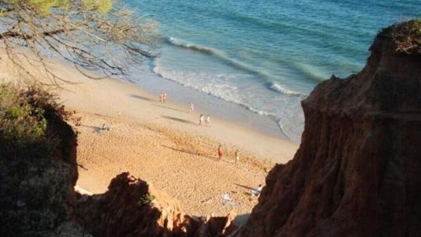 A beach with clear blue water, sandy shore, and rocky cliffs.
