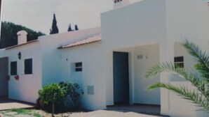 A modern building with a flat roof and white walls. There are small windows and a door visible.