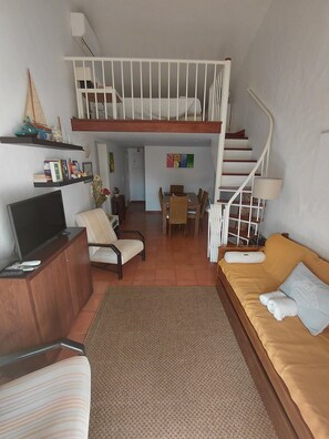 A loft-style living space with a dining area, a TV, a sofa, and a staircase leading to an upper level.