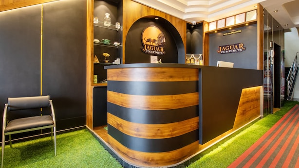 A reception desk with a wooden finish and a Jaguar logo. There is a chair to the left of the desk. - Treebo Jaguar Comforts, 3 Kms From Mahatma Gandhi Park (Chikkamagaluru)