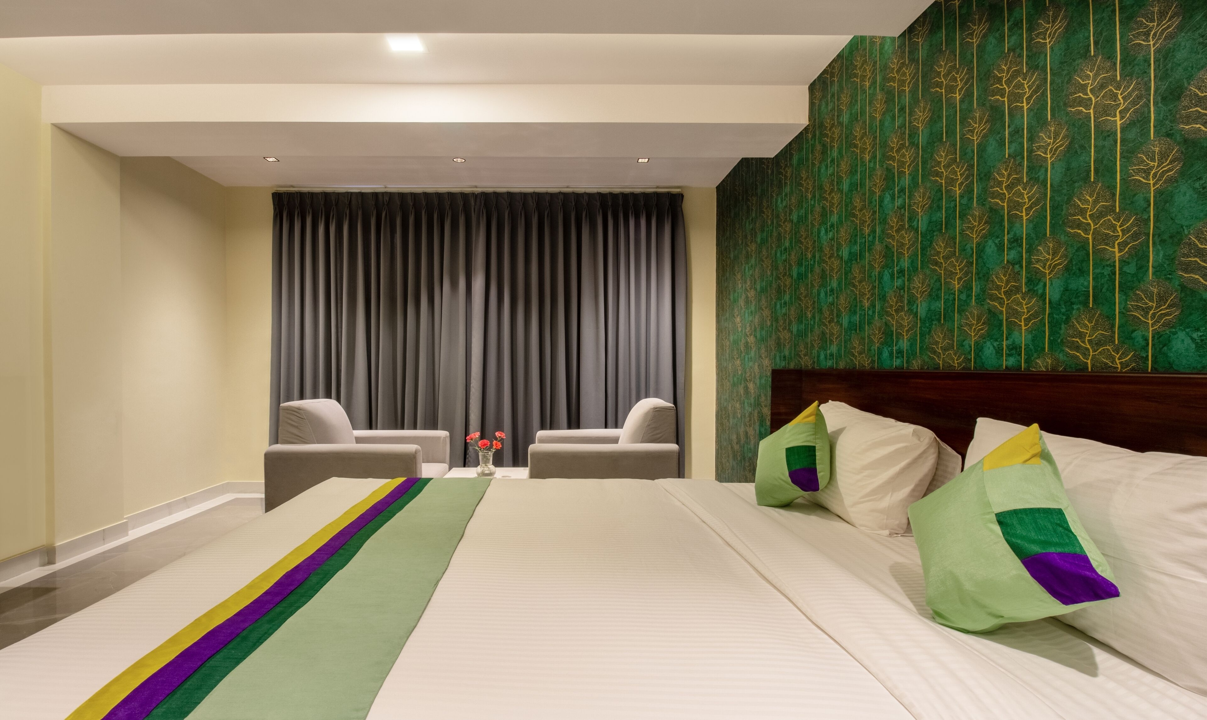 A hotel room with a large bed, two armchairs, a wooden headboard, and a green patterned wall.