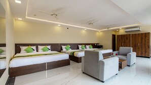 A hotel room with two beds, a sofa, a chair, a wardrobe, and a ceiling fan. - Treebo Jaguar Comforts, 3 Kms From Mahatma Gandhi Park (Chikkamagaluru)