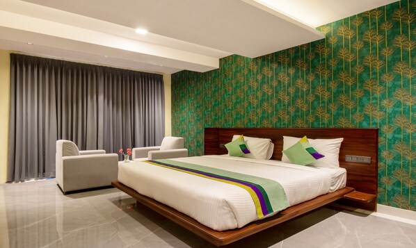 A modern hotel room with a large bed, a wooden headboard, a grey curtain, and a green patterned wall. - Treebo Jaguar Comforts, 3 Kms From Mahatma Gandhi Park (Chikkamagaluru)