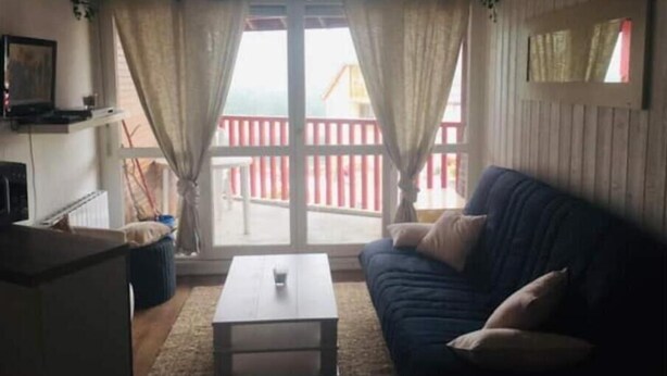 Un salon avec un canapé, une table basse et une vue sur un balcon rouge, visible à travers de grandes fenêtres.