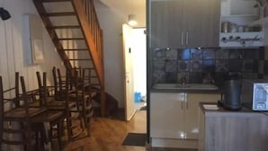 Une cuisine avec des meubles de rangement en bois, un évier et une cuisinière. Un escalier mène à une autre pièce.