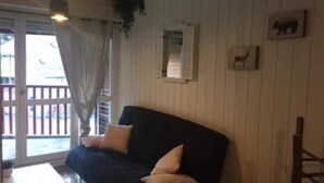 Une pièce avec un canapé de couleur sombre, une chaise en bois, une petite table et une fenêtre donnant sur l’extérieur.