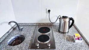 Een keuken met een ingebouwde kookplaat, waterkoker, spoelbak en een doosje theezakjes.