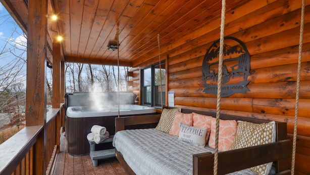 A log cabin with a hot tub, a bed with pillows, and a wooden deck.