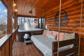 Une cabane en rondins avec un jacuzzi, un lit avec des oreillers et une terrasse en bois.