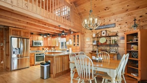 A wooden cabin interior with a kitchen, dining area, and a chandelier.