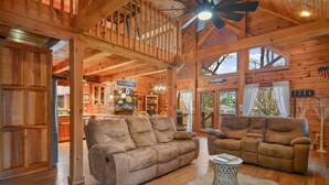 A spacious wooden cabin interior with two sofas, a dining area, and a kitchen.