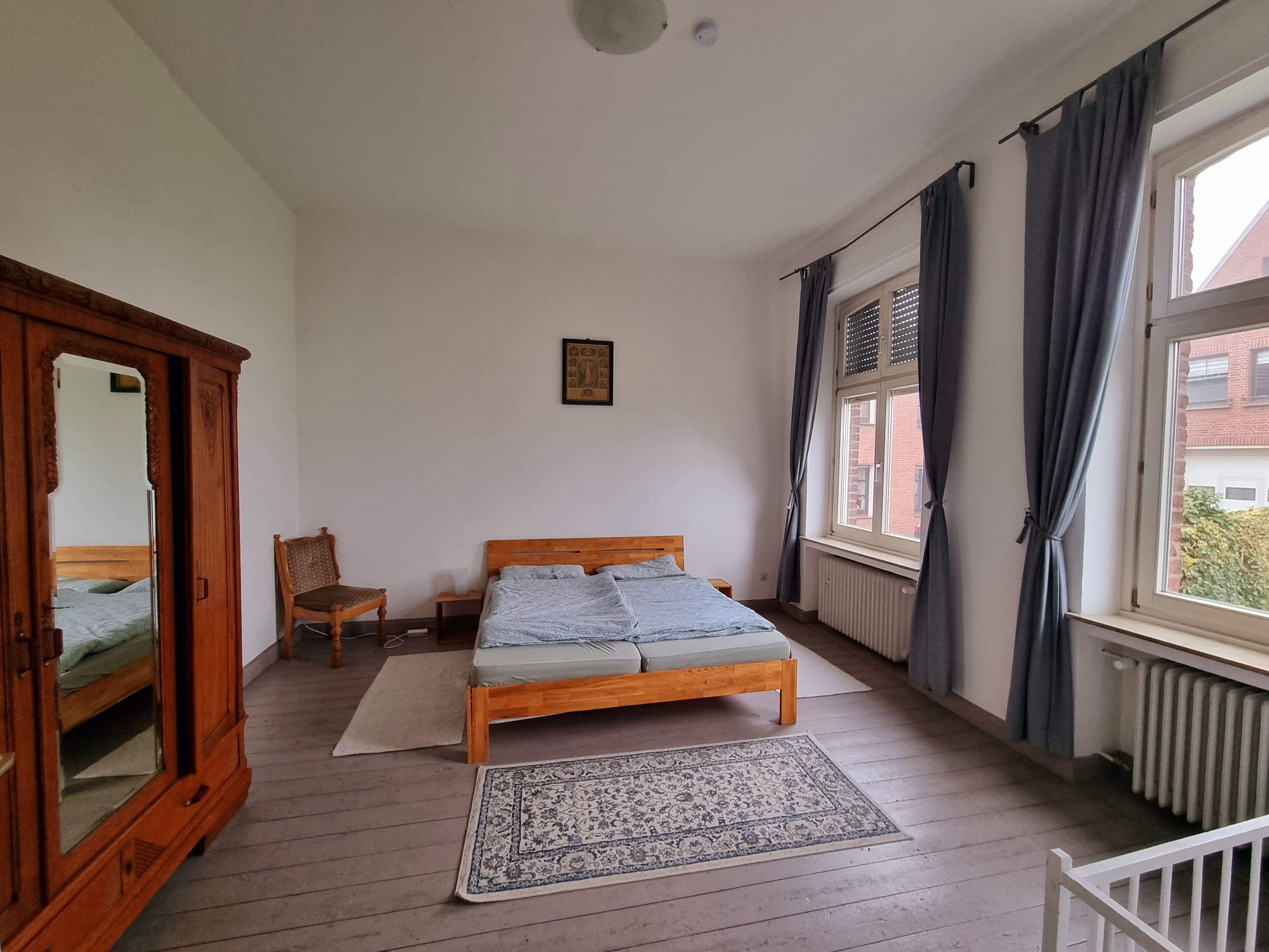 Un dormitorio con cama de madera, una silla, un armario y una ventana con cortinas.