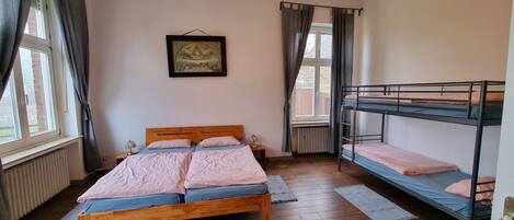 Ein Zimmer mit einem hölzernen Bett, einem Etagenbett, einem Heizkörper und einem gerahmten Bild an der Wand.