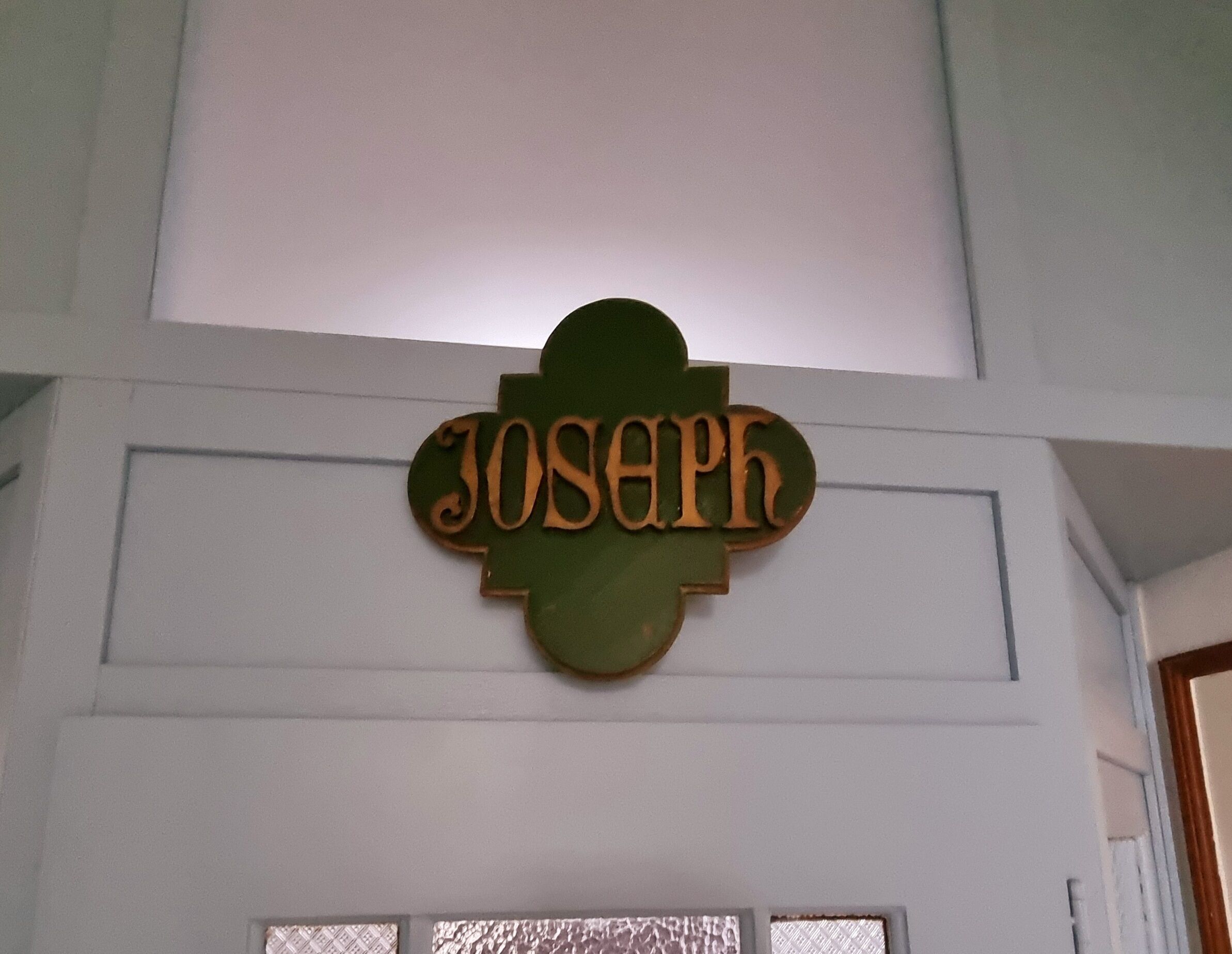 En træskilt med navnet "Joseph" monteret på en hvid væg.