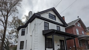 A two-story house with a white exterior and black trim, a covered porch, and a brick chimney. - Bright and Spacious 5 BR Home Close to downtown. Pet-Friendly! (Cincinnati)