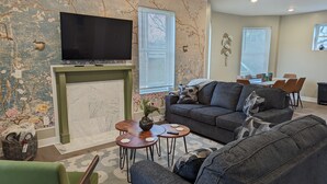 A living room with a fireplace, a sofa, a TV, and a dining area with chairs and a table. - Bright and Spacious 5 BR Home Close to downtown. Pet-Friendly! (Cincinnati)
