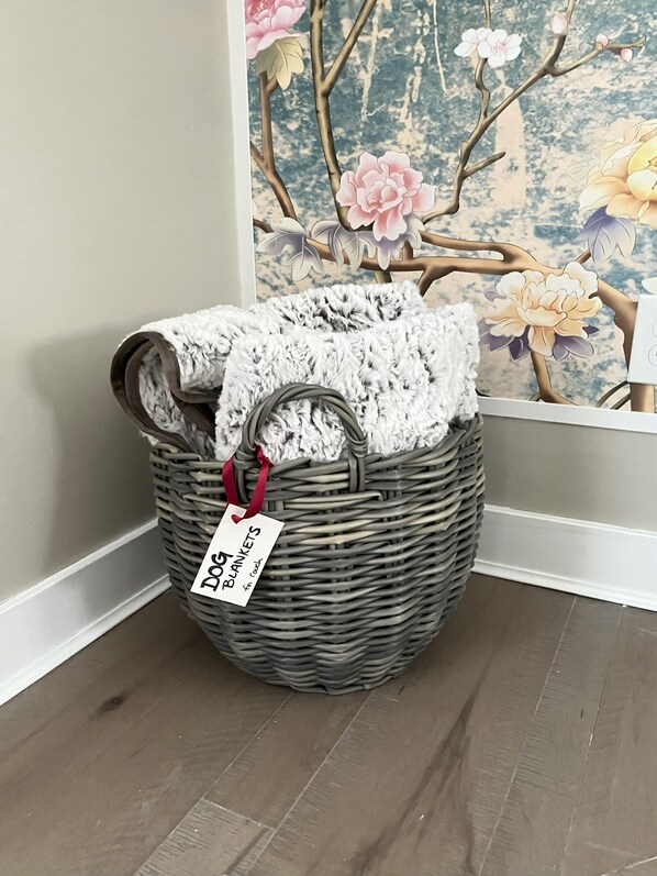 A wicker basket with a tag labeled "Dog Blankets" on a wooden floor.