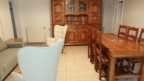Uma sala de jantar com uma mesa e cadeiras de madeira, uma poltrona bege e um armário de madeira com portas de vidro.