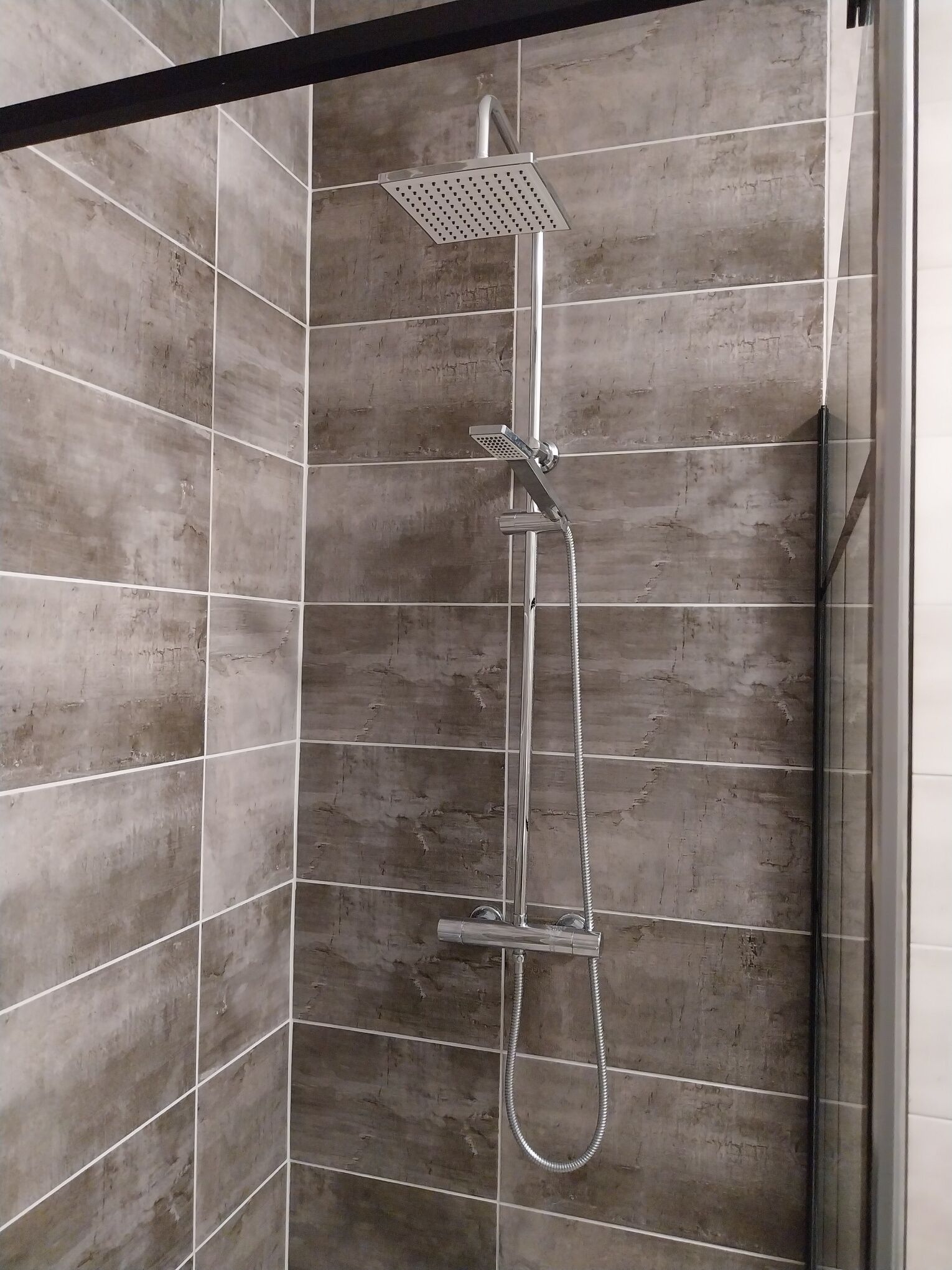 A shower with a handheld showerhead and a fixed overhead showerhead in a tiled shower enclosure.