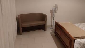 Ein Schlafzimmer mit einem Bett, einem Holznachttisch, einer weißen Lampe, einem beigen Sofa und einem Gemälde an der Wand.