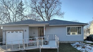 A single-story house with a garage, a front porch with a ramp, and a small front yard with snow patches. - Charming Family 1-level and pet-friendly Home (Austin)