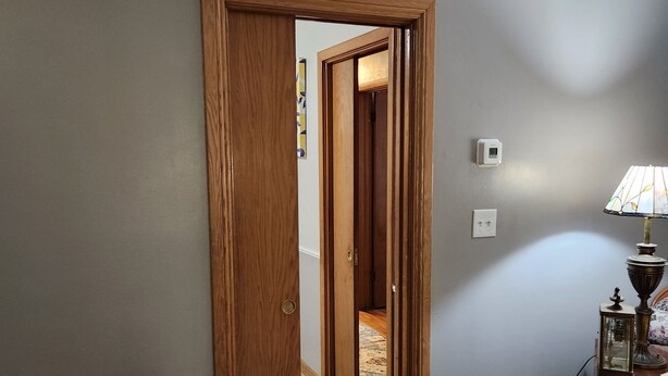 A room with a wooden door leading to a hallway, a bed with a floral bedspread, a lamp, and a small table with a decorative item. - Charming Family 1-level and pet-friendly Home (Austin)