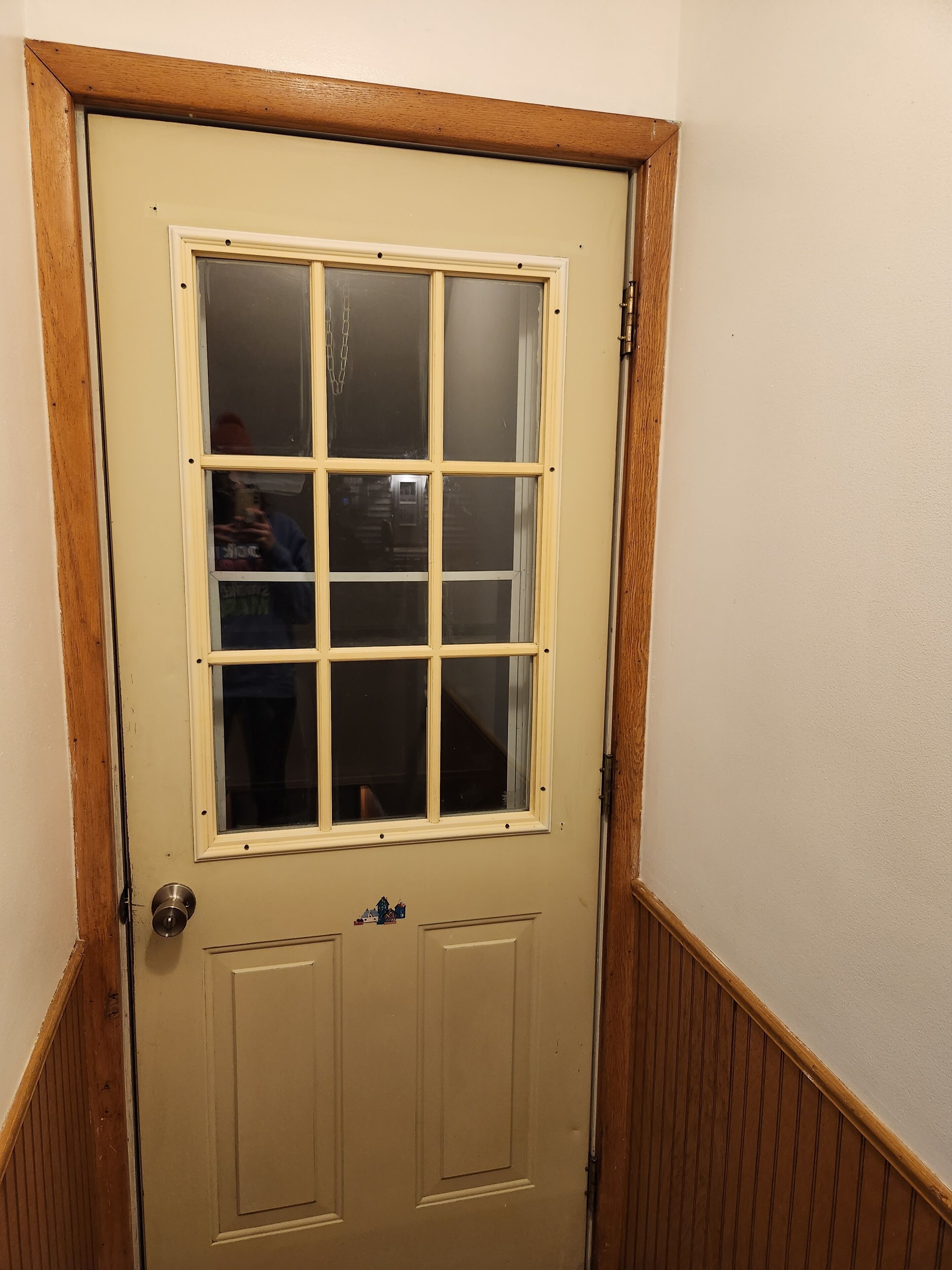 A beige door with a window and a small doorbell.