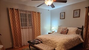 A bedroom with a bed, a bench, a nightstand with a lamp, and a ceiling fan. - Charming Family 1-level and pet-friendly Home (Austin)