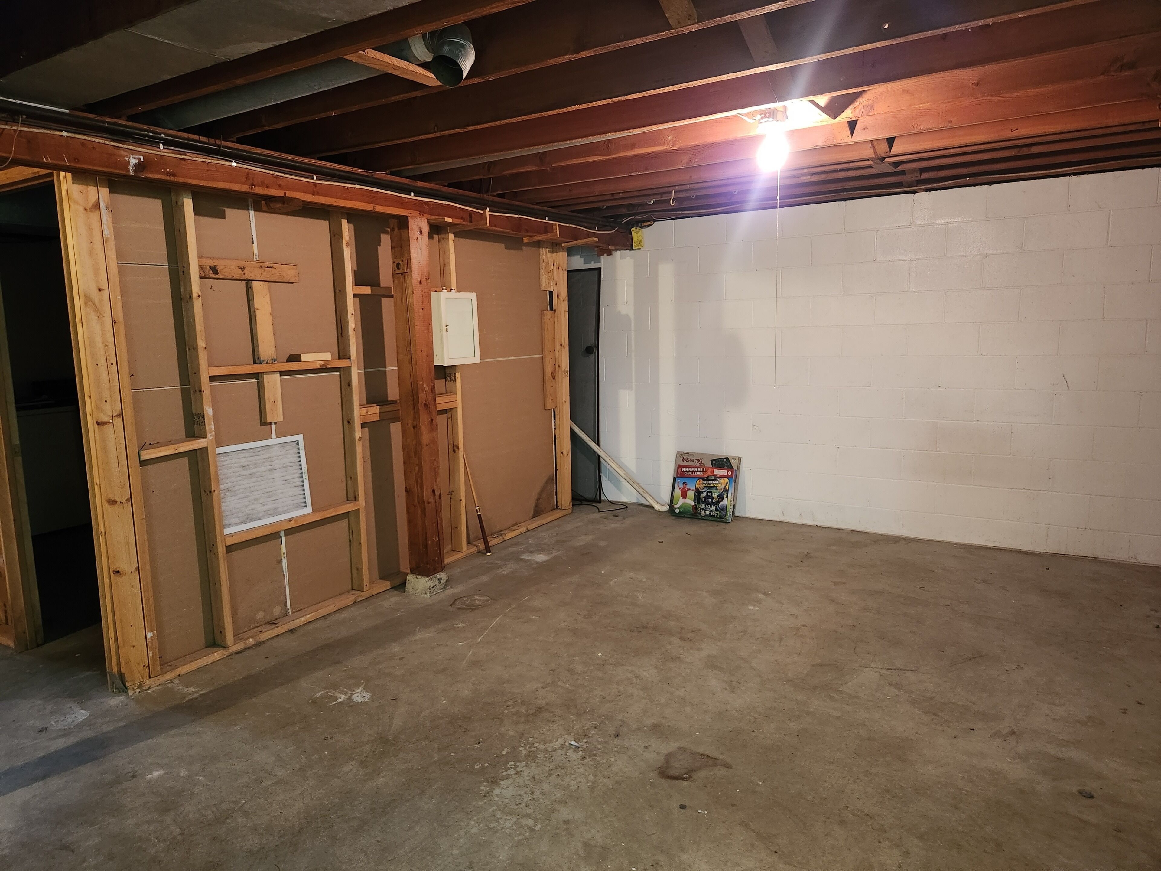 Un sous-sol avec une structure en bois, un plancher en béton et un mur en briques blanches.