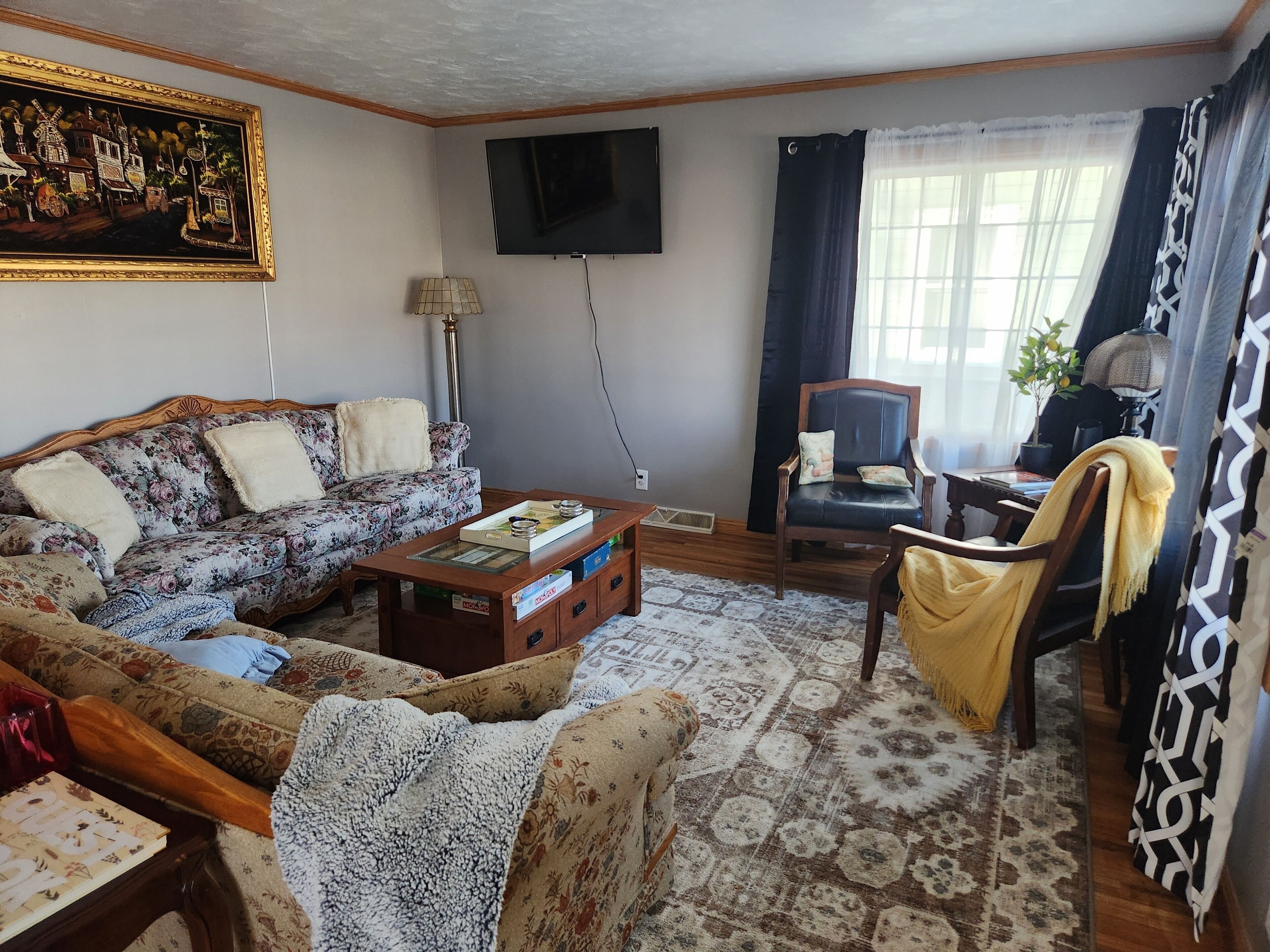 Ein Wohnzimmer mit Sofa, Sessel, Couchtisch und einem an der Wand befestigten Fernseher.