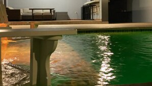 A pool area with a lounge chair and a table, a compass wall decoration, and a tiled pool edge.