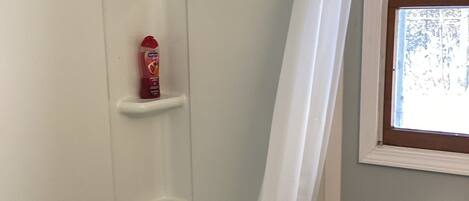 Une salle de bain avec une baignoire blanche, un rideau de douche, un porte-rouleau de papier toilette et une fenêtre donnant sur des arbres.