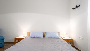 Un dormitorio con una cama, dos mesitas de noche con lámparas, un sillón azul y una lámpara fijada a la pared.
